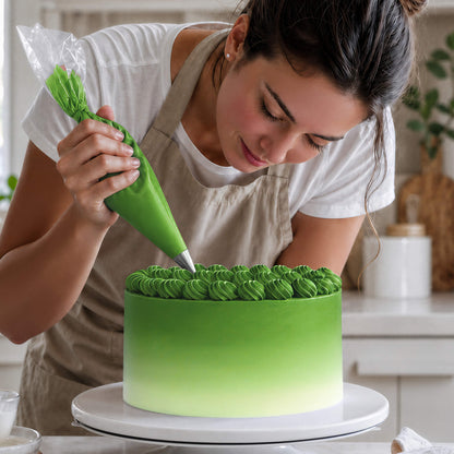 Frau spritzt Buttercreme-Tupfen in Grün auf eine Torte mit Farbverlauf von Grün zu Weiß